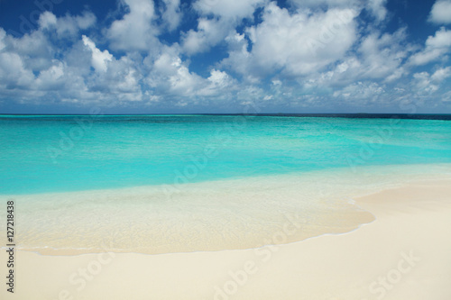 Tropical beach. Ocean waves and cloudy sky background. White san