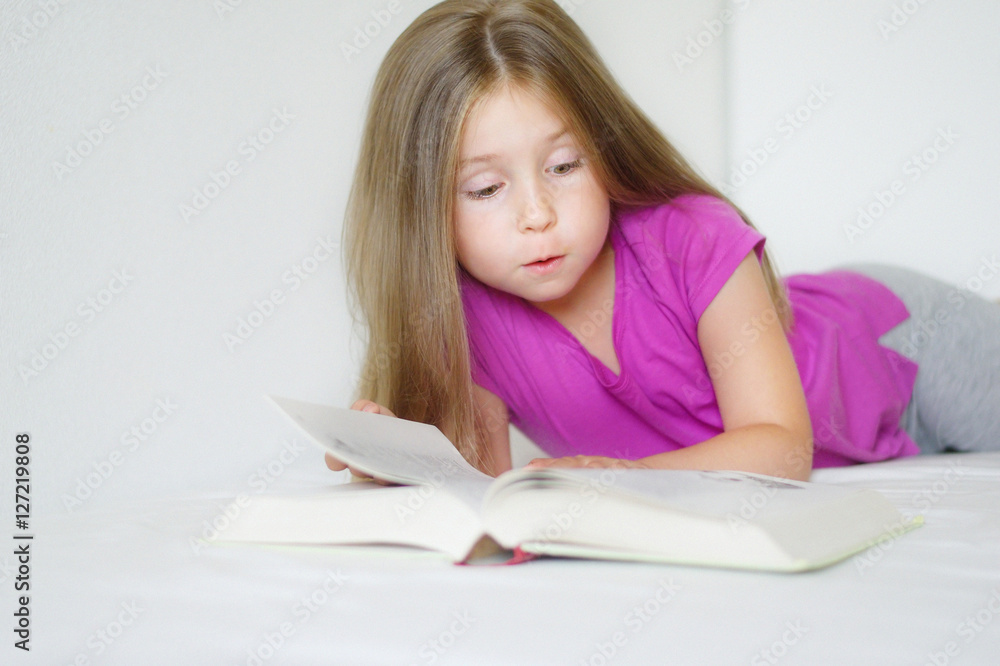Adorable little girl lying on the bed and reading a book Adorable little girl lying on the bed and reading a book