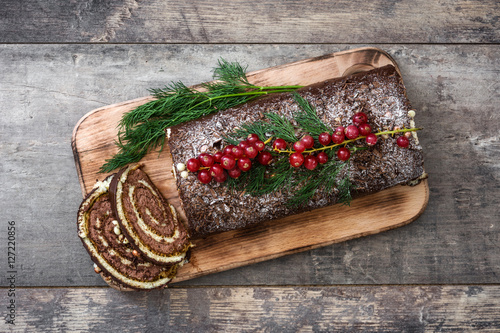 Chocolate yule log christmas cake with red currant on wooden background.copyspace
 photo