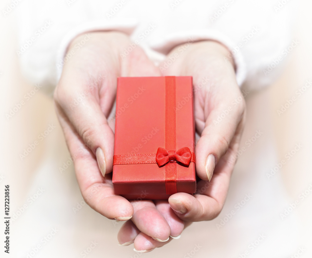 Hands of a woman showing a gift: little red box with a ribbon. Selective focus. Hands of a woman showing a gift: little red box with a ribbon. Selective focus.
