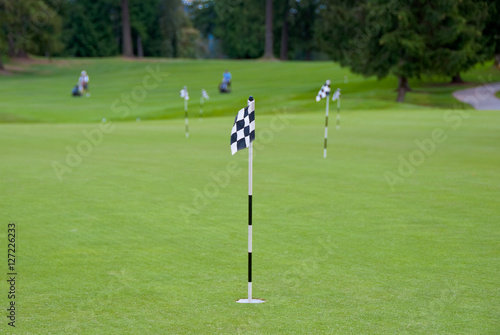 Putting area over a blurred green. Shallow depth of field. Focus on the first flag.