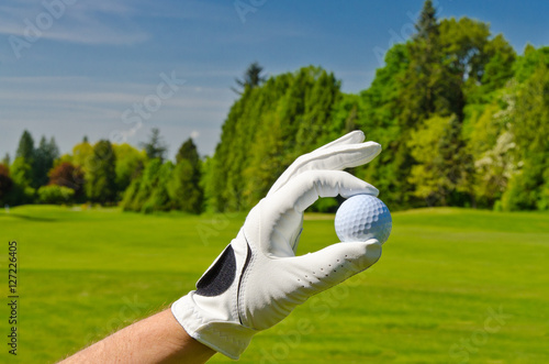 hand placing golf ball on tee over beautiful golf course with blue sky