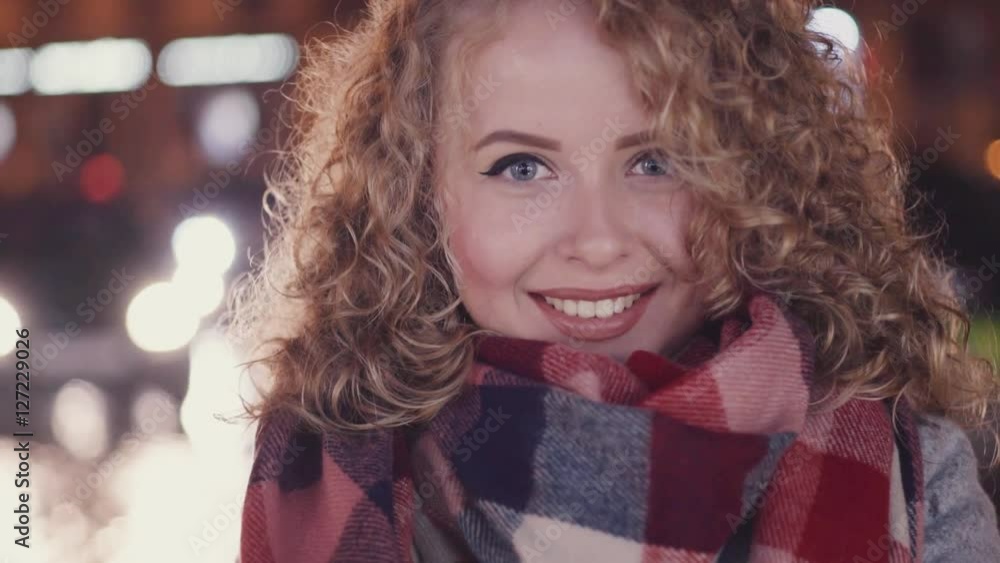 Beautiful woman with gorgeous eyes standing by the city street smiling towards the camera. Cars passing by. City lights around. Lonely atmosphere. Chilly weather. Female portrait. Beautiful woman with gorgeous eyes standing by the city street smiling towards the camera. Cars passing by. City lights around. Lonely atmosphere. Chilly weather. Female portrait.