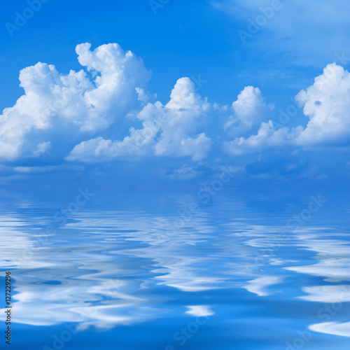 Clouds in the bright blue sky are reflected in a surface of wate