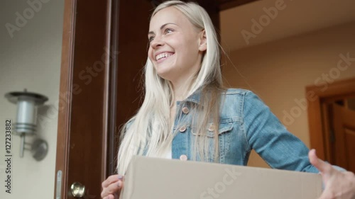 Smiling Homeowner Receives Postal Parcel and Signs Electronic Signature Deivce. While Standing in the Open Doorway. Shot on RED Cinema Camera in 4K (UHD). photo