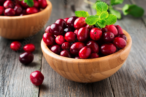 Fresh juicy cranberries in a bamboo bowl on the old wooden background. Selective focus.