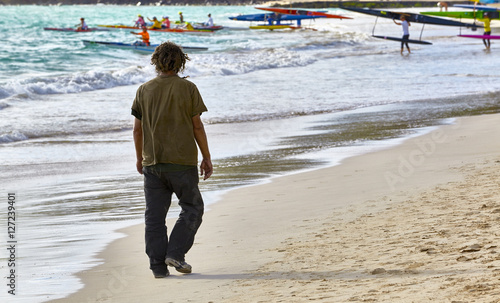 man walking on the beach with tourists and canoes