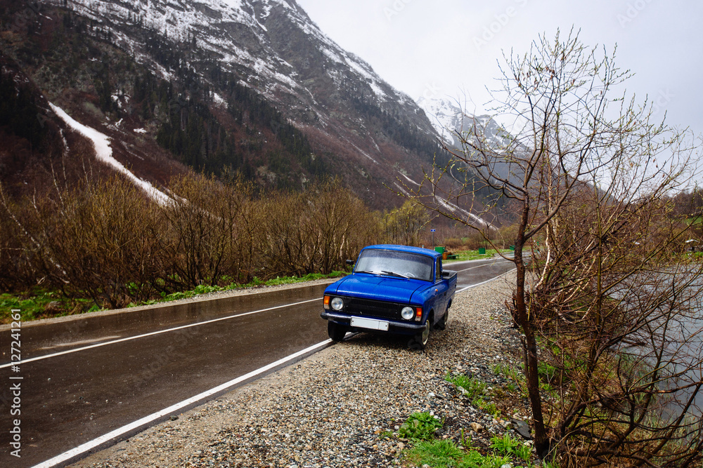 A blue car stands on the side of the mountains in the background