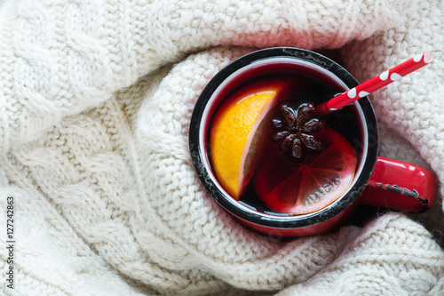 Christmas and winter traditional hot beverage. Mulled wine in red mug with spice wrapped in warm green scandinavian sweater.