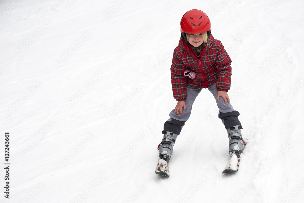 Naklejka premium Happy child girl enjoying vacation in winter resort. Little girl skiing in mountains. Active sportive toddler wearing helmet learning to ski. Winter sport for family. Skier racing in snow.