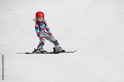 Happy child girl enjoying vacation in winter resort. Little girl skiing in mountains. Active sportive toddler wearing helmet learning to ski. Winter sport for family. Skier racing in snow.