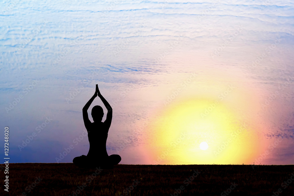 Silhouette of woman practicing yoga at sunrise