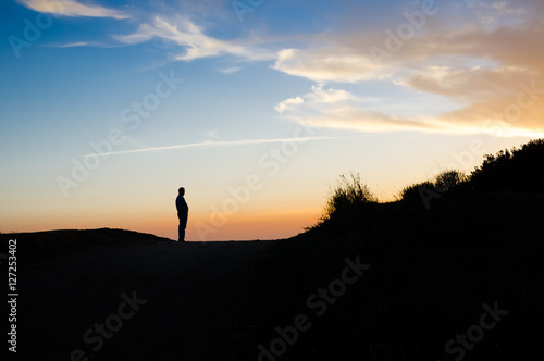 A silhouette of a middle aged man watching a sunset on a mountain plateau.