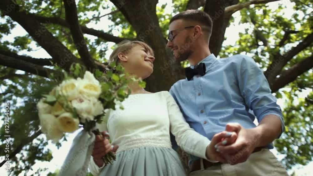 Bottom view. Young beautiful newlyweds kiss against a background of green tree in the park Bottom view. Young beautiful newlyweds kiss against a background of green tree in the park