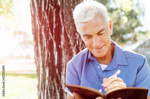 Senior man sittingin park while reading book photo