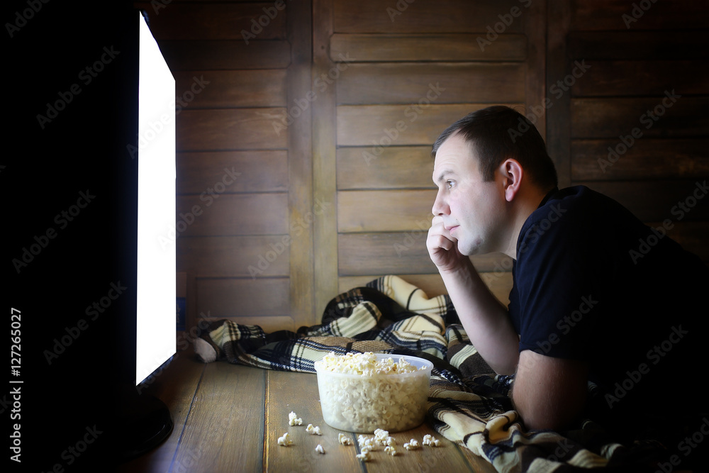 Naklejka premium young man watching television at home on the floor