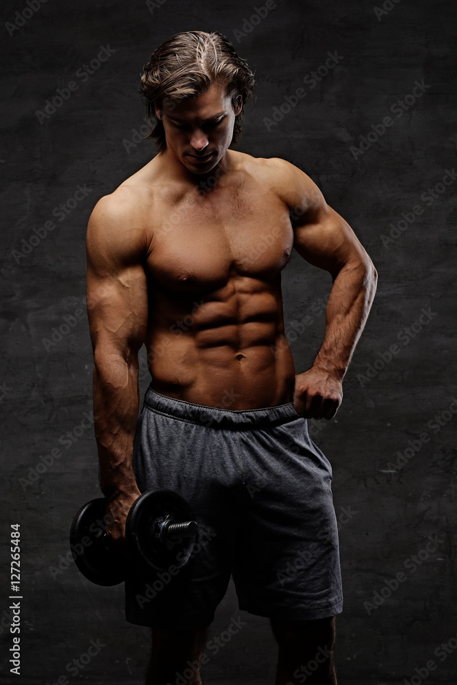 The shirtless abdominal male holds dumbbell.