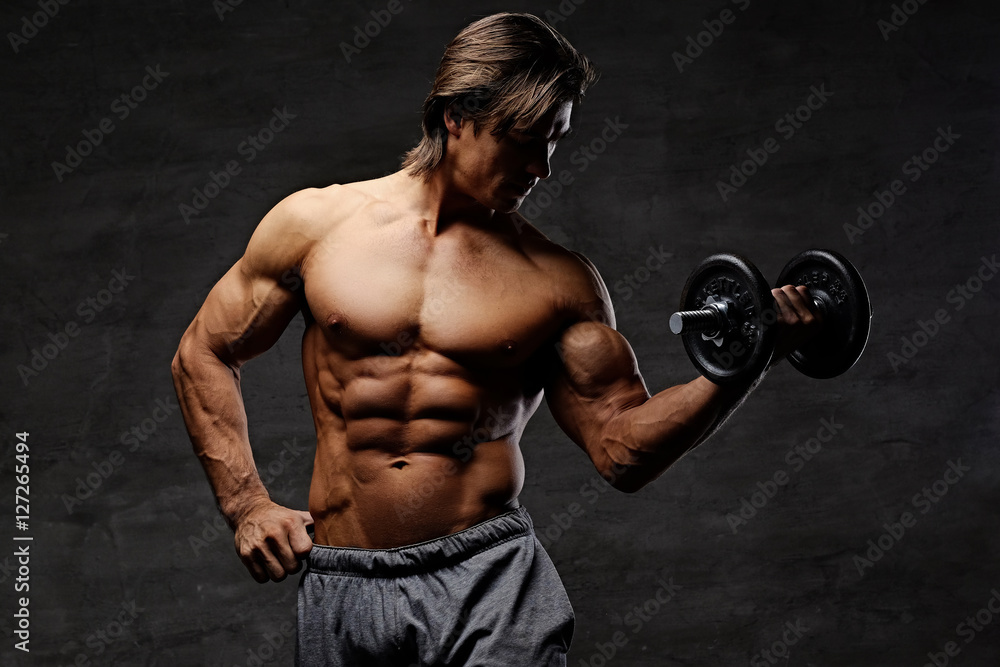 The shirtless abdominal male holds dumbbell.