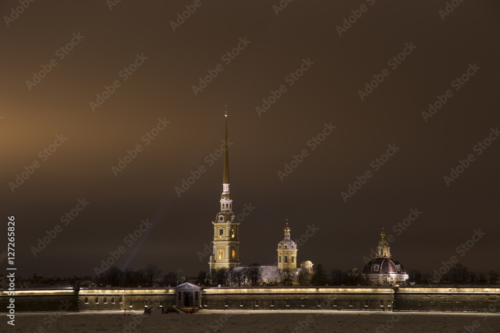 Петропавловская крепость. Вид с дворцовой набережной через Неву во льду зимой вечером. Луч прожектора.