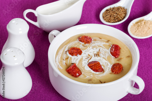 delicious Beer and cream spicy Soup with Kielbasa Sausage sprinkled with cumin in white soup cup on magenta table mat with salt and pepper shakers, authentic recipe, close-up