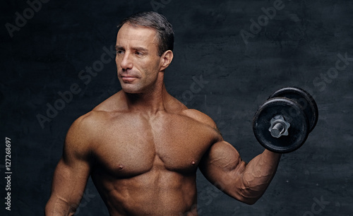 Shirtless middle age male holds dumbbell. © Fxquadro