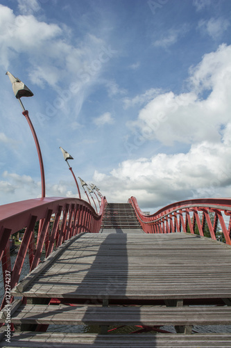 Wooden stairway with red banister in the blue sky with clouds in the daylight