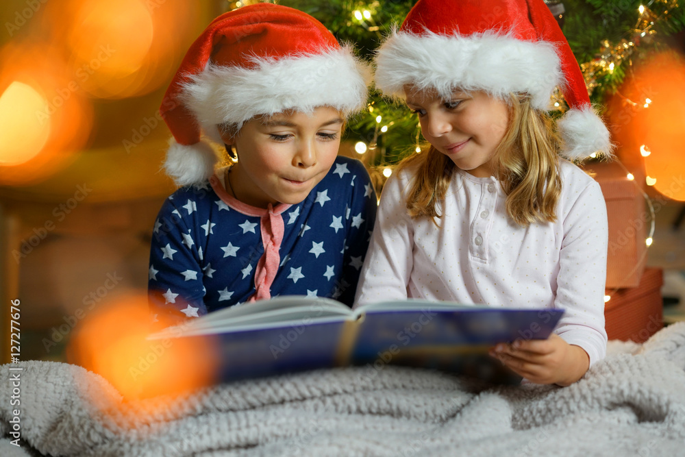 Kids reading book by Christmas tree Kids reading book by Christmas tree