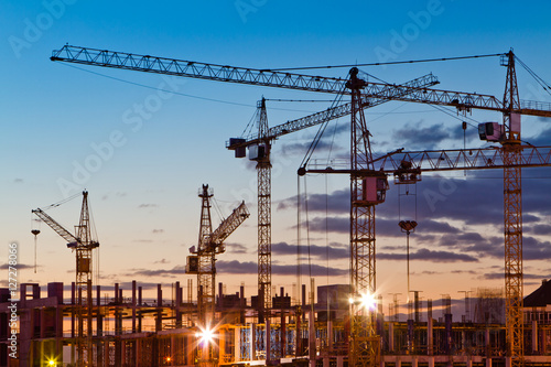 Silhouettes of tower cranes against the evening sky. House under construction. Industrial skyline