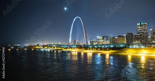 St. Louis, Missouri, USA - view of the illuminated city at night with the Gateway Arch monument and the Mississippi River with passing ship - Timelapse with zoom out 