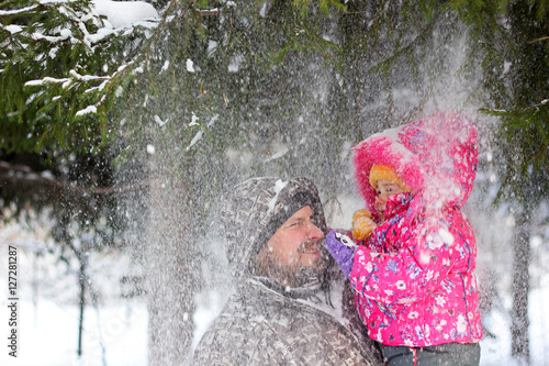 Father together with the daughter under falling snow flakes from