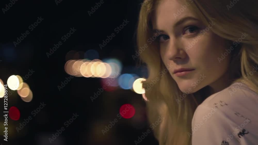 Young blonde beautiful girl walking at the night city with bokeh light background and fashion looking at the camera close-up Young blonde beautiful girl walking at the night city with bokeh light background and fashion looking at the camera close-up