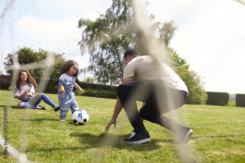 Parents squat to play football with their young daughter