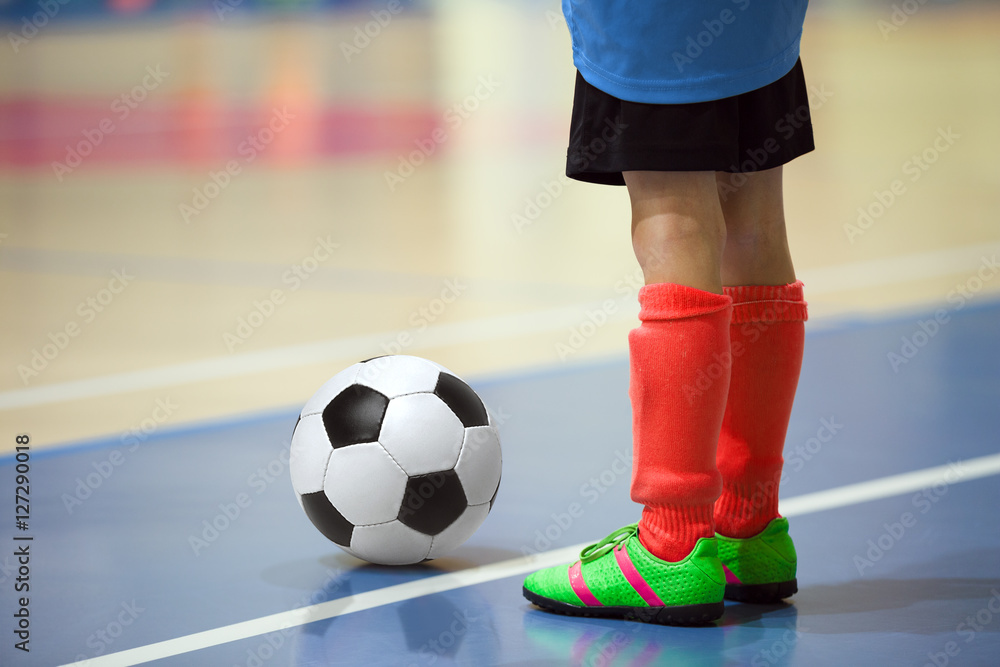 Fototapeta premium Football futsal training for children. Indoor soccer young player with a soccer ball in a sports hall. Player in blue and red uniform. Sport background.