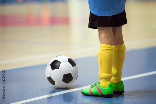 Football futsal training for children. Indoor soccer young player with a soccer ball in a sports hall. Player in blue and yellow uniform. Sport background.