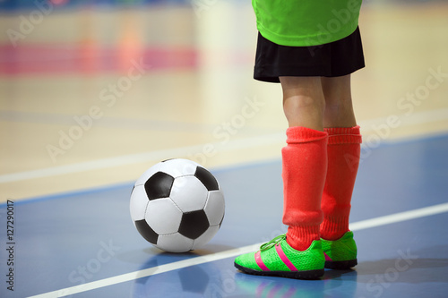 Football futsal training for children. Indoor soccer young player with a soccer ball in a sports hall. Player in yellow and red uniform. Sport background.
