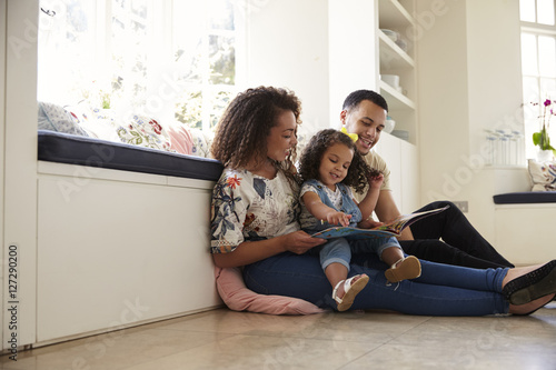 Parents and their daughter sitting on the floor reading book photo
