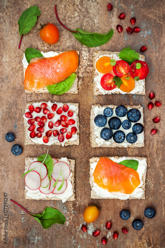 Bruschetta crostini appetizers mix set with various toppings. Variety of small sandwiches with salmon, tomatoes, ricotta, blueberries and pomegranate seeds on crisp rye bread