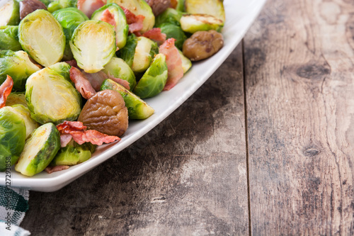 Brussels sprouts with chestnuts and bacon on wooden table 