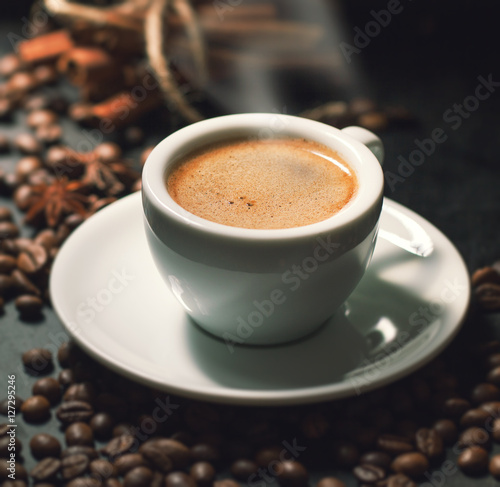 Fresh tasty espresso cup of hot coffee with coffee beans on dark