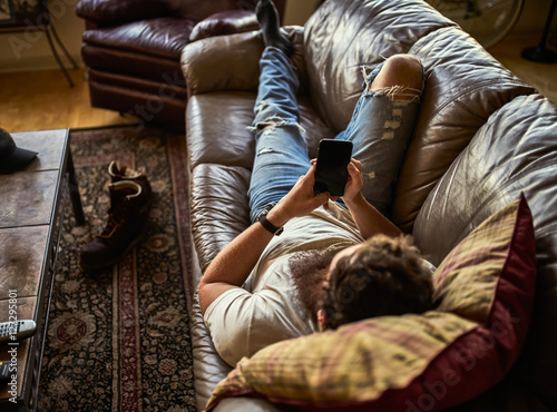 bearded guy relaxing on couch at home using smart phone © Joshua Resnick