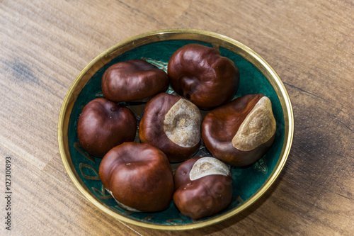 Small green pot of chestnuts lying on wooden floor. 