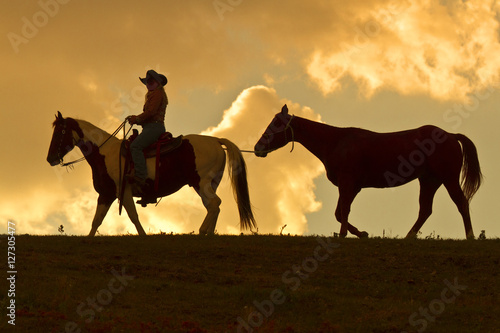 Silhouette of cowgirl leading a horse at sunset