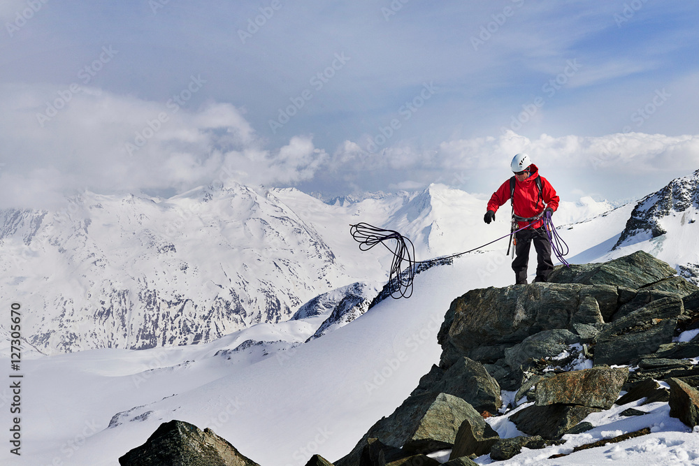 Man on top of snow covered mountain throwing climbing rope, Saas Fee,  Switzerland Stock Photo
