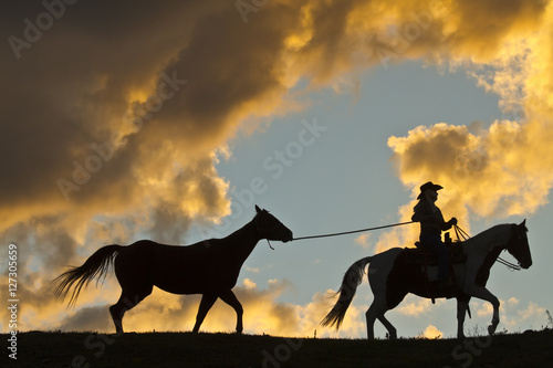 Cowgirl leading a horse at sunset in silhouette