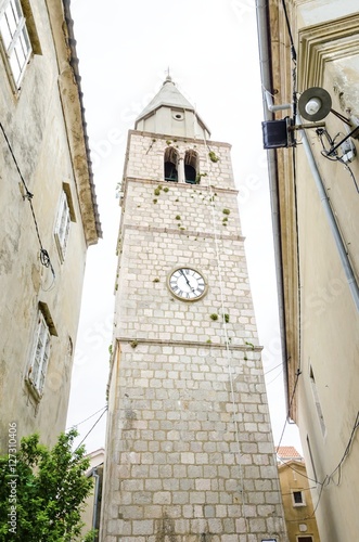 The renaissance bell tower of the Parish Church of the Assumption of the Blessed Virgin Mary in Vrbnik town, Krk, Croatia. A medieval spire with a clock and historic religious monument and landmark. photo