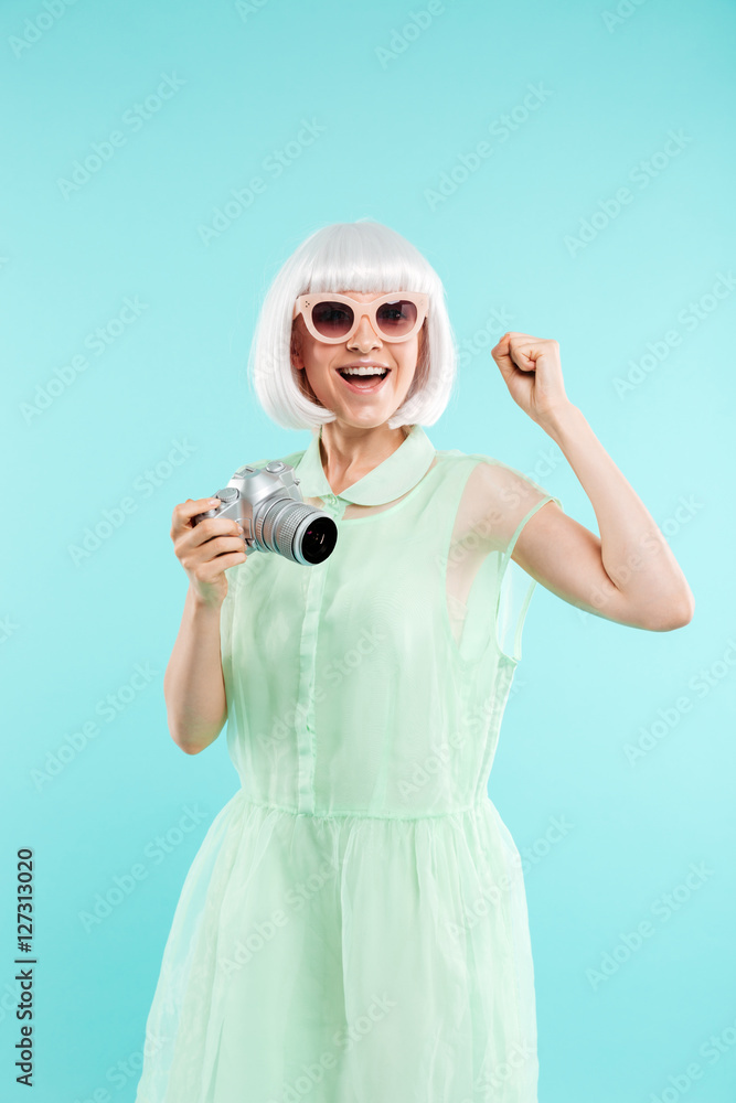 Cheerful young woman photographer holding photo camera and celebrating