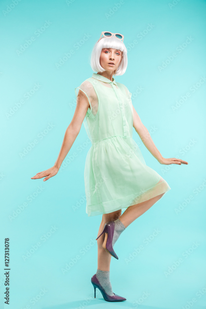 Charming blonde young woman in dress standing on one leg