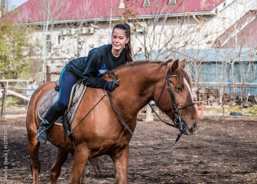 Young beautiful brunette girl rides a horse on a warm and sunny autumn day. Portrait of a pretty young woman on the horse, wearing tall boots and gloves. Young beautiful brunette girl rides a horse on a warm and sunny autumn day. Portrait of a pretty young woman on the horse, wearing tall boots and gloves.