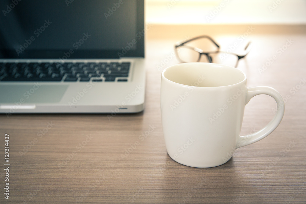 Close up view of a work desk interior with a laptop computer, A coffee cup on working table with glass. Vintage tone photo of work desk with computer and coffee cup Close up view of a work desk interior with a laptop computer, A coffee cup on working table with glass. Vintage tone photo of work desk with computer and coffee cup