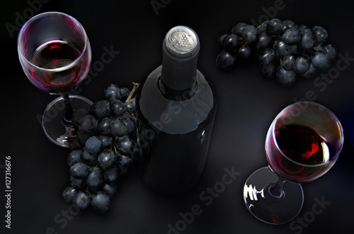 bottle of red wine,  wine glasses and grapes on black table